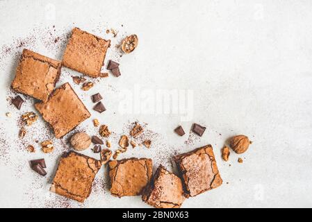 Vista superior de pastel de brownie recién horneado hecho en casa, con nueces, chocolate y cacao en polvo sobre fondo blanco rústico. Foto de stock