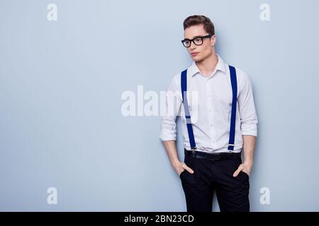 Retrato de un joven penisivo atractivo en camisa blanca y gafas, de pie sobre el fondo de luz pura y con tirantes violetas