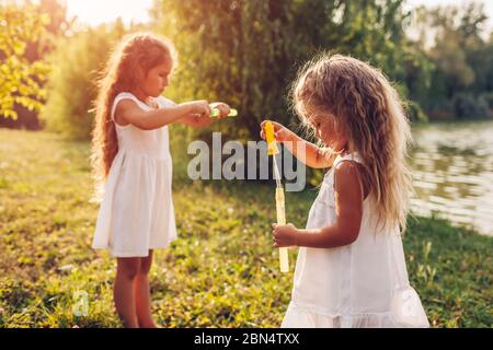 Hermanas de chicas pequeñas soplando burbujas en el parque de primavera. Los niños se divierten jugando al aire libre. Actividades infantiles