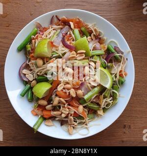 Wok plato nudddles con verduras cacahuetes y lima. Cuenco blanco sobre mesa de madera, tiro desde arriba. Comida saludable Foto de stock
