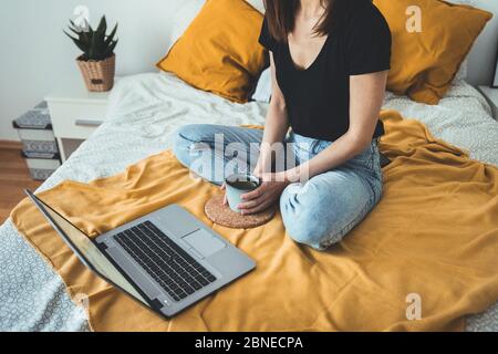 Mujer joven relajante y beber taza de café caliente o té utilizando el ordenador portátil en bedroom.woman comprobar las aplicaciones sociales y el trabajo