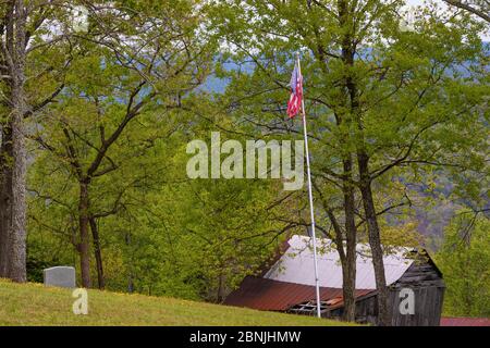 Un pequeño cementerio en una colina de campo con una bandera estadounidense atterada que cuelga de un poste de bandera.