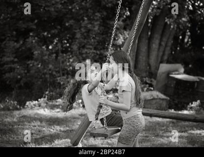 Dos chicas hermosas felices jugando en swing y sonriendo en el cálido día de verano