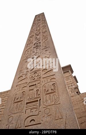 Gran obelisco egipcio antiguo alto en el templo de Luxor con tallas jeroglíficas aisladas sobre fondo blanco Foto de stock