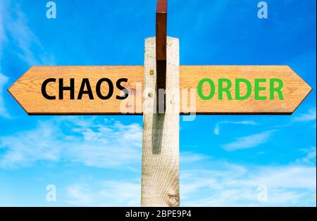 Cartel de madera con dos flechas opuestas sobre el azul claro del cielo, el caos versus mensajes de orden Foto de stock