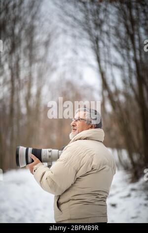 Hombre Senior dedicar tiempo a su pasatiempo favorito - Fotografía - tomando fotos con su cámara digital exterior/DSLR y un gran lente telefoto Foto de stock