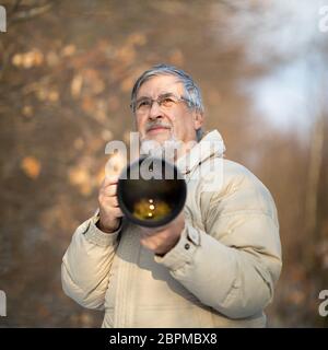 Hombre Senior dedicar tiempo a su pasatiempo favorito - Fotografía - tomando fotos con su cámara digital exterior/DSLR y un gran lente telefoto Foto de stock