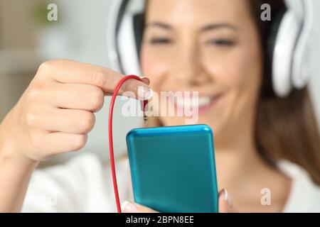 Cerca de una mujer feliz mano enchufando el conector jack de auriculares al teléfono inteligente. Foto de stock