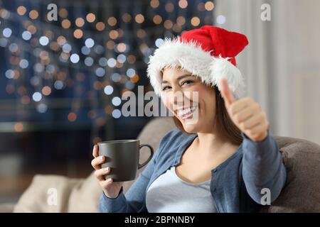 Feliz mujer con pulgares hacia arriba en la navidad sentados en un sofá en el salón en casa Foto de stock