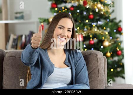 Mujer feliz en navidad con pulgares arriba sentados en un sofá en el salón en casa Foto de stock
