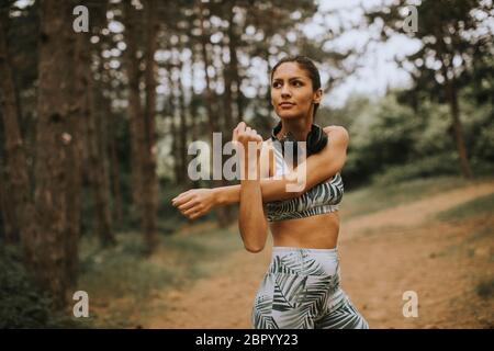 Mujer joven estirándose y respirando aire fresco en medio del bosque mientras hace ejercicio