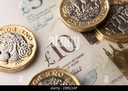 Una libra de moneda con la cara de la reina Isabel II y 5 y 10 libras de billetes en el fondo Foto de stock