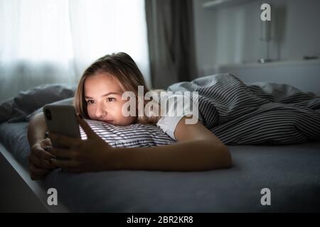 Bonita, mujer joven durmiendo en su cama con su teléfono celular cerca de ella. Concepto de adicción de smartphone/móvil en cama. Foto de stock