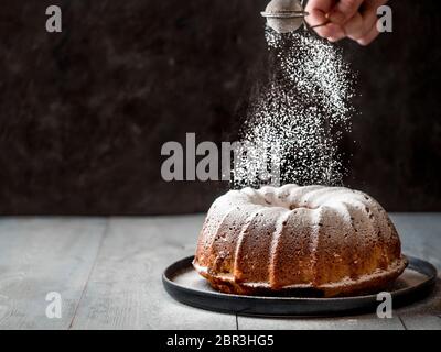 La mano de la mujer roció azúcar glaseado sobre la torta fresca de muffin. El azúcar en polvo cae en la torta de muffin perfecta fresca. Copiar espacio para texto. Ideas y recetas para Foto de stock