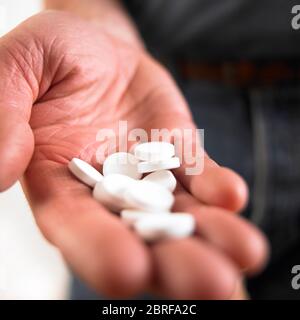 Mano masculina sosteniendo tabletas blancas de medicina Foto de stock