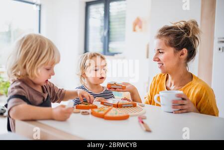Madre con dos niños pequeños en el interior en el dormitorio jugando con juguetes.