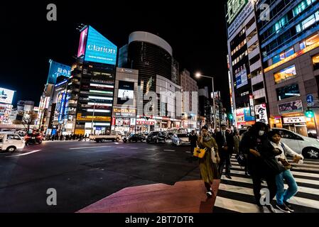 Shibuya, Japón - 1 de abril de 2019: Famoso cruce en el centro de la ciudad con luces publicitarias de neón y gente caminando por la noche en Tokio Foto de stock