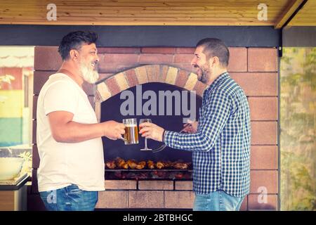 Amigos multirraciales masculinos divertirse cocinando carne en la parrilla mientras beben alcohol Foto de stock