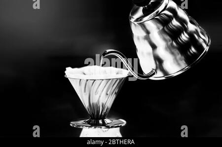 Café de goteo verter sobre el café con agua caliente que se vierte de una caldera, fondo negro Foto de stock