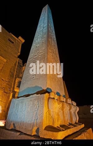 Gran obelisco egipcio antiguo alto en el templo de Luxor con esculturas jeroglíficas iluminadas por la noche Foto de stock