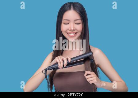 Joven mujer asiática alisando el cabello y sintiéndose bien Foto de stock