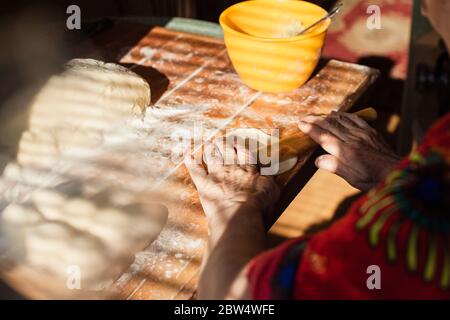 La mujer mayor se ha puesto a rodar la masa en la harina con el rodillo en la cocina de su casa Foto de stock