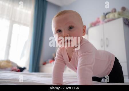 Lindo bebé niña de pie en la cama hacer caras divertidas, cara enojada, llorando por la mañana Foto de stock