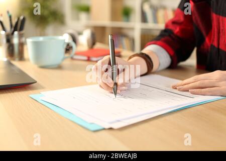 Primer plano de las manos de la niña de estudiante llenando el formulario de solicitud sentado en un escritorio en casa Foto de stock