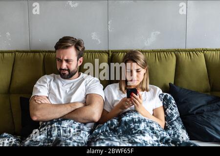 Confundirse pareja joven tener un argumento acerca de teléfono móvil mientras está acostada en la cama
