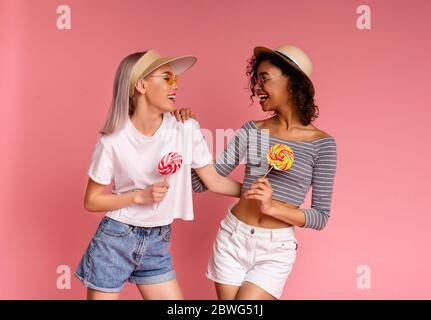 Jóvenes Girlfriends alegres en ropa de verano posando con Lollipops sobre fondo rosa Foto de stock