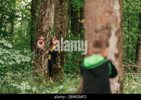 Niño pequeño y linda chica jugando escondidas y buscan en el bosque, pasando buen tiempo en la naturaleza de primavera.