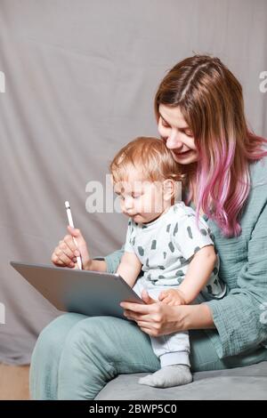 Quédese en casa, mamá trabaja remotamente en un ordenador portátil, cuidando a su hijo. Una joven madre en licencia de maternidad está tratando de trabajar como una mujer independiente Foto de stock