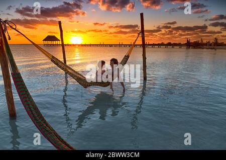 Madre e hija relajándose en una hamaca en la playa durante el atardecer en la Isla Holbox, Cancún, México