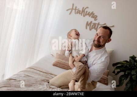 Padre agachándose en la cama cosquillando a su hijo pequeño