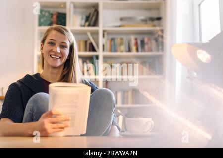 Retrato de una joven feliz leyendo un libro en casa