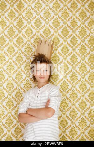 Retrato de un niño parado en una pared con corona de cartón Foto de stock