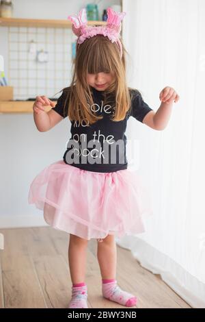 Niña pequeña, en casa jugando disfrazada con un traje de bailarina con tutú rosa tul, calcetines y antenas