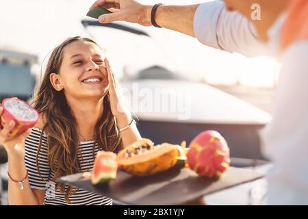 Niño feliz comiendo frutas tropicales mientras juega con el padre - papá y la hija que se divierten juntos el fin de semana día soleado
