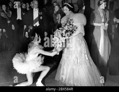 La Reina recibe un ramo de flores de Beryl Groom, a su llegada al teatro, para una actuación de la Escuela de Ballet Wells de Sadler. A la izquierda está Earl of Lytton, el presidente del cuerpo de Gobierno del Viejo Vic y Sandler's Wells. Foto de stock