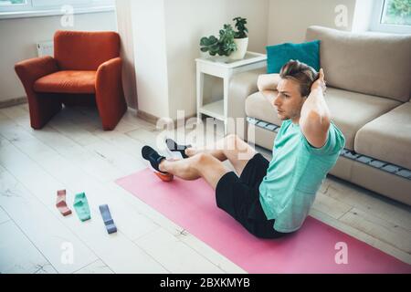 Hombre caucásico con cerdas haciendo ejercicios de abs en casa en una alfombra de yoga usando algunas bandas elásticas