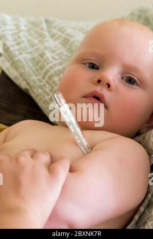 Mamá mide la temperatura de su bebé pequeño con un termómetro de mercurio Foto de stock