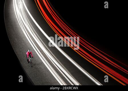 Mujer Cíclica en chaqueta rosa brillante a caballo en la bicicleta en la carretera nocturna con coches senderos de luz. Estilo de vida saludable y concepto de deporte activo urbano.