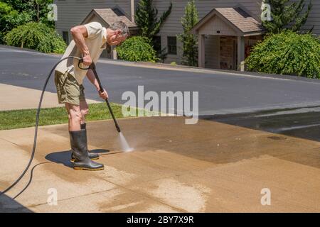 Hombre caucásico mayor rociando camino de concreto con agua a alta presión spray para limpiarlo Foto de stock