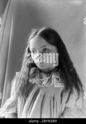 Una fotografía inglesa clásica de estilo victoriano tardío o Edwardiano temprano de una niña, mostrando la moda y el estilo de la época.
