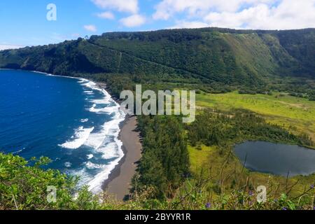 Increíble paisaje del valle de Waipio con acantilado de origen volcánico en el azul brillante del océano Pacífico con playa de arena negra y valle con ne residencial