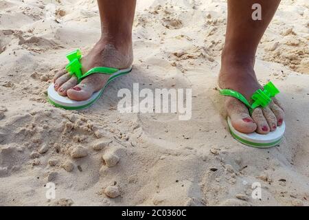 Pies femeninos en sandalias en una playa de arena