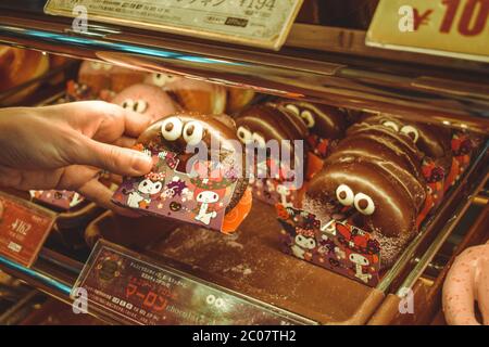 Mujer mano sosteniendo un lindo donut japonés con ojos sobre un plato con otros donuts de carácter Foto de stock