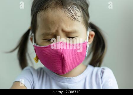 Un niño triste y estresado mirando hacia abajo tosiendo de una enfermedad mala, usando una máscara para protegerla de su ambiente. Foto de stock