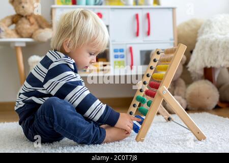 Lindo niño pequeño, jugando con mostrador, colorido abacus, aprendiendo contando solo en casa Foto de stock