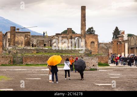 Turistas en un día lluvioso en el Foro Romano (Foro Civile di Pompeya) mirando al Templo de Júpiter en la histórica ciudad de Pompeya, Italia